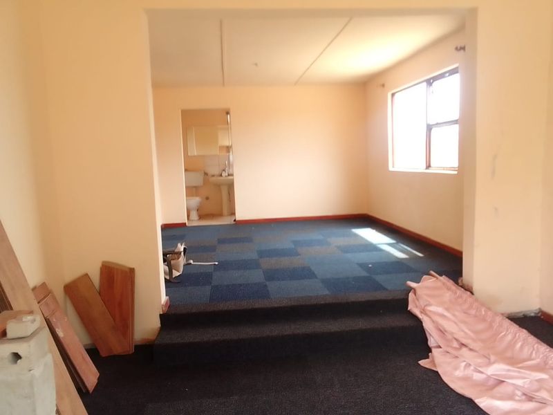 An empty bedroom featuring a raised platform area, blue carpeted flooring, and an attached en-suite bathroom.