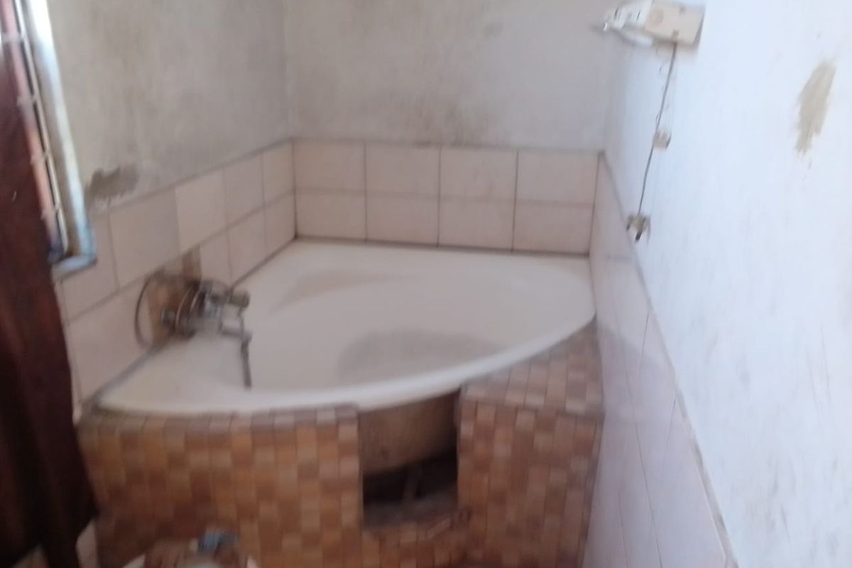A bathroom featuring a corner bathtub with tiled surround, currently requiring significant renovation and finishing of wall surfaces and fixtures.