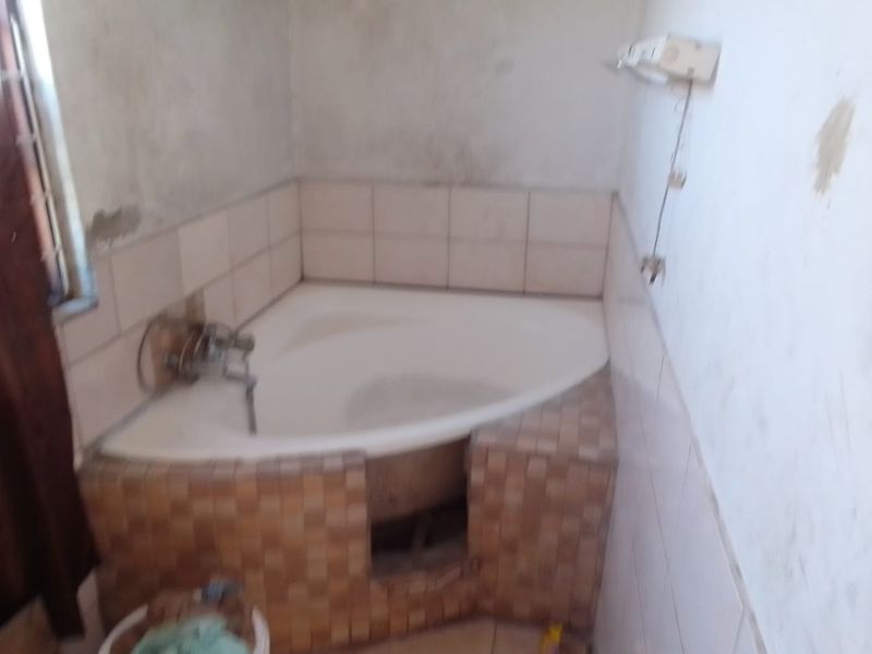 A bathroom featuring a corner bathtub with tiled surround, currently requiring significant renovation and finishing of wall surfaces and fixtures.