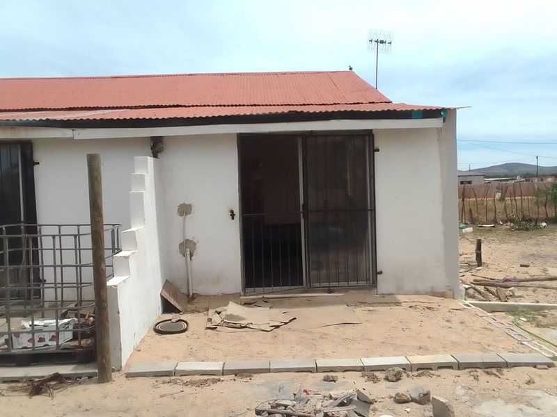 Rear view of a residential property featuring a corrugated metal roof, sliding glass door with security gate, and unfinished exterior wall surfaces.