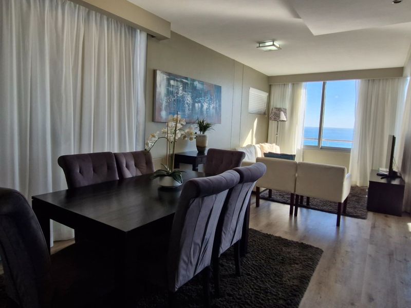 Spacious open-plan living and dining area featuring laminate flooring, modern recessed lighting, and direct access to a balcony with ocean views.