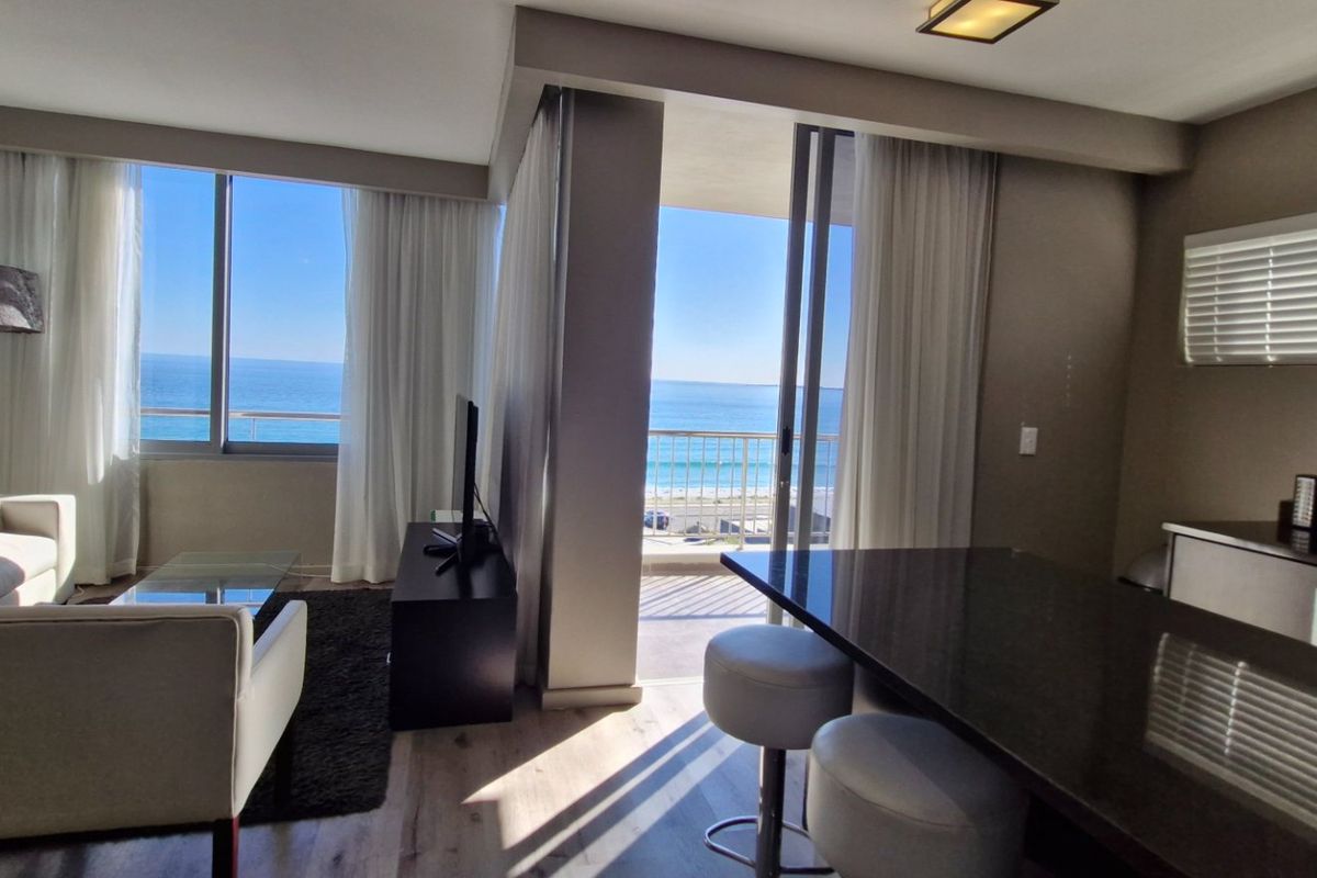 Open-plan living and kitchen area featuring modern finishes, laminate flooring, and large sliding doors opening onto a balcony with ocean views.
