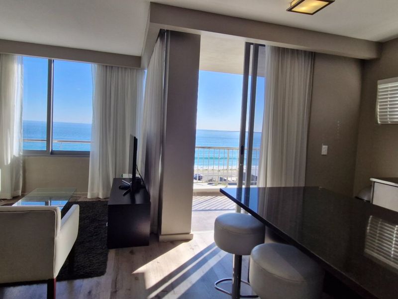 Open-plan living and kitchen area featuring modern finishes, laminate flooring, and large sliding doors opening onto a balcony with ocean views.