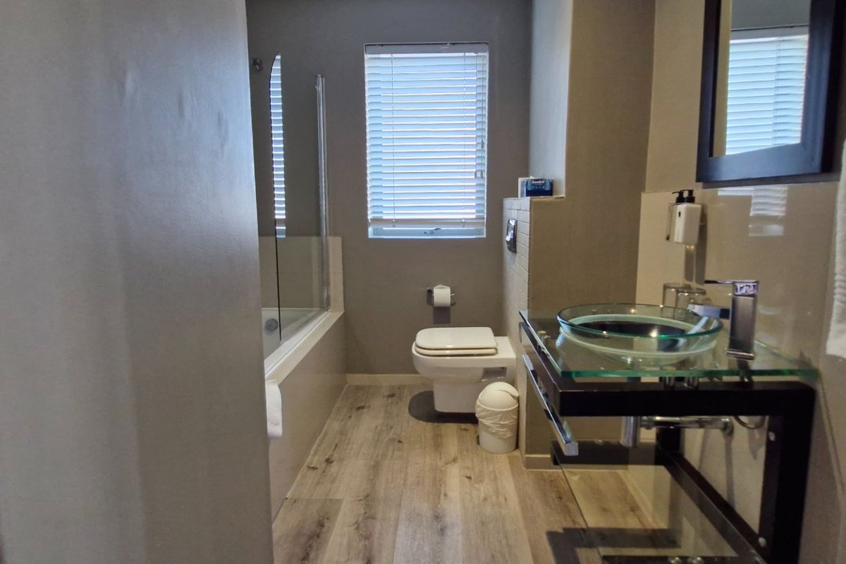 A modern bathroom featuring a glass vessel sink, wall-mounted vanity, bathtub with glass screen, and wood-look laminate flooring.