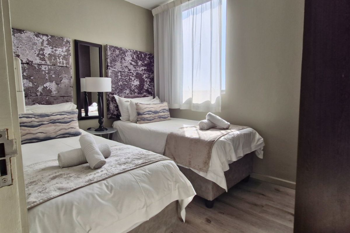 A compact bedroom featuring laminate flooring and a window with sheer curtains, currently configured with two single beds.