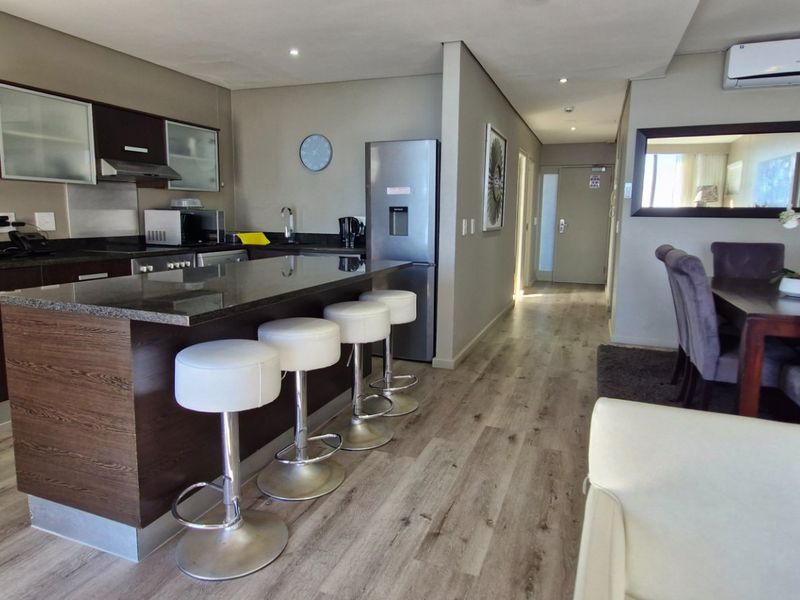Open-plan living and kitchen area featuring dark wood cabinetry, granite countertops, a central island, and modern laminate flooring throughout.