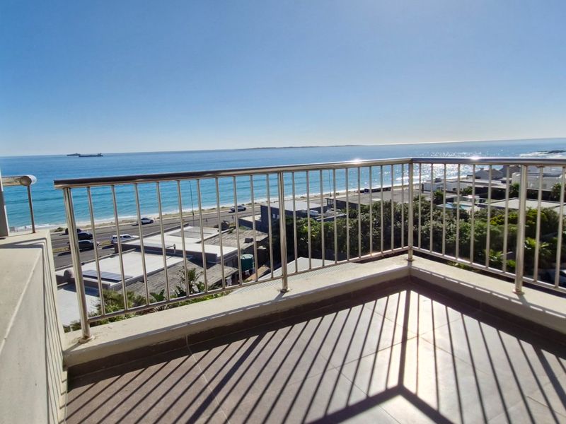 A private balcony featuring a stainless steel balustrade and tiled flooring, offering expansive, unobstructed ocean and coastal views.