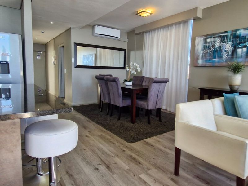 Modern open-plan living and dining area featuring laminate flooring, a sleek kitchen breakfast bar, and a wall-mounted air conditioning unit.