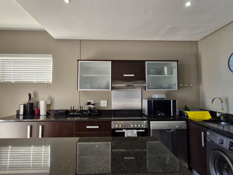 Modern kitchen featuring dark wood cabinetry, granite countertops, stainless steel appliances, and recessed downlighting, offering a functional and contemporary cooking space.