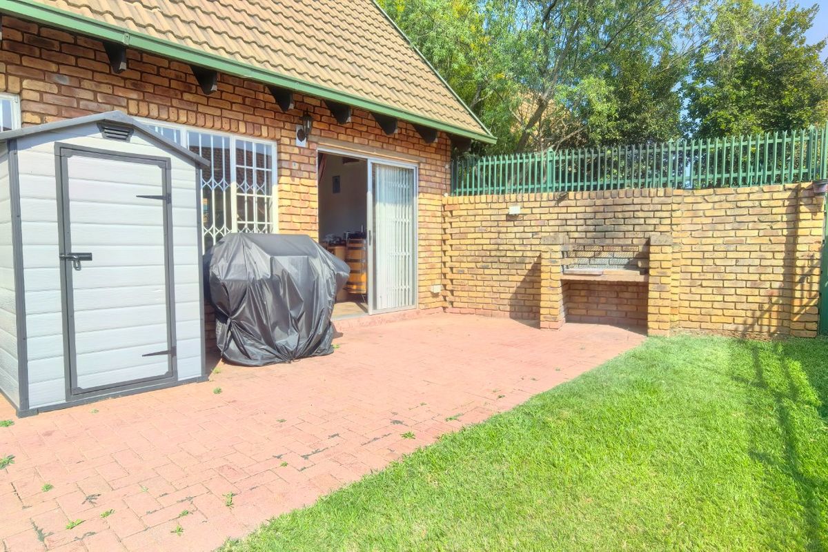 Rear exterior view of a townhouse featuring a paved patio area, built-in brick braai, and a small private garden with boundary walling.