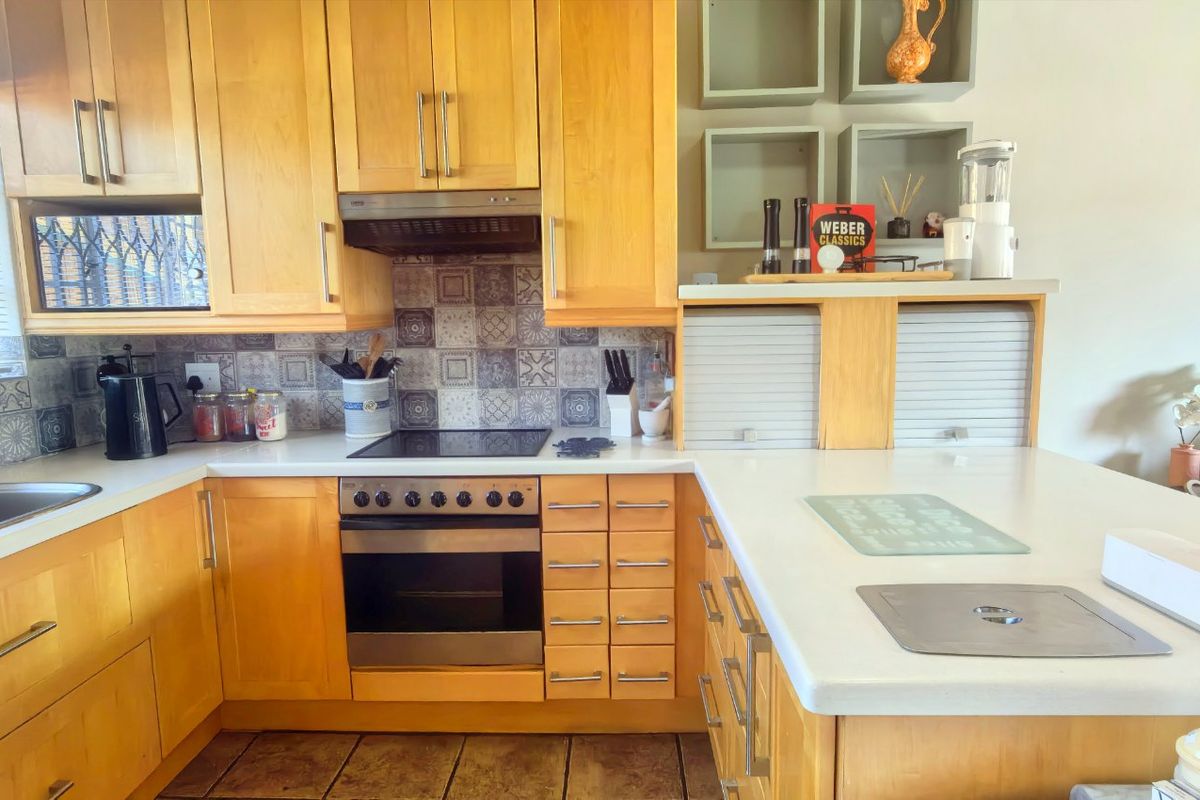 A functional kitchen featuring light wood cabinetry, a tiled backsplash, built-in oven and hob, and ample counter space with a convenient appliance garage.