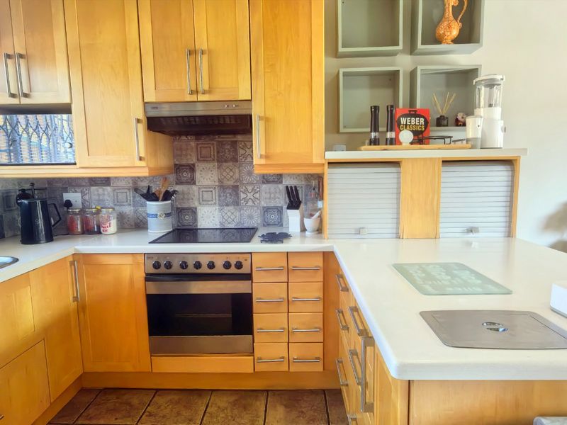 A functional kitchen featuring light wood cabinetry, a tiled backsplash, built-in oven and hob, and ample counter space with a convenient appliance garage.