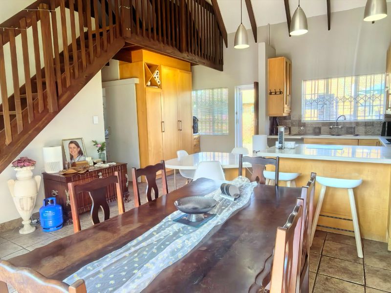 Open-plan living and dining area featuring a wooden staircase, exposed timber beams, and a functional kitchen with built-in cabinetry and island.