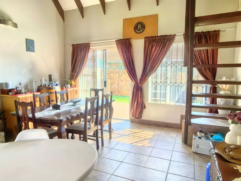 Open-plan living and dining area featuring tiled floors, exposed timber rafters, and a wooden staircase leading to an upper level with garden access.