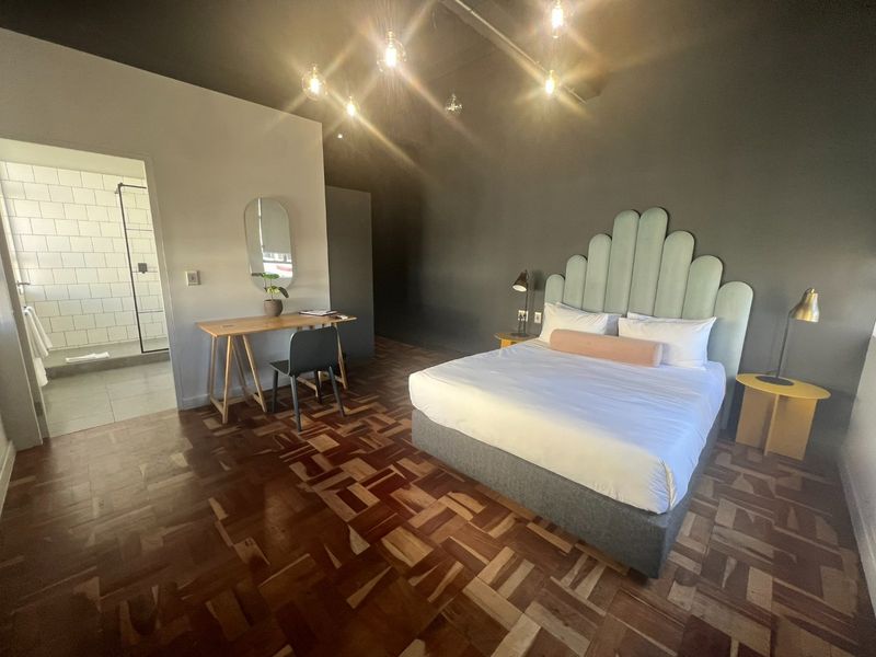 Spacious bedroom featuring rich parquet flooring, dark accent walls, exposed ceiling lighting, and direct access to an en-suite bathroom with a walk-in shower.