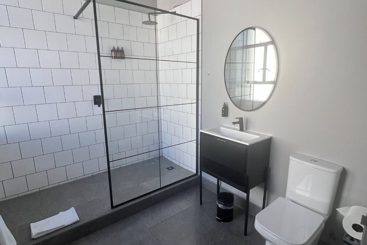 Modern bathroom featuring a walk-in shower with black-framed glass screen, subway tiling, vanity basin, and toilet with contemporary dark floor tiles.