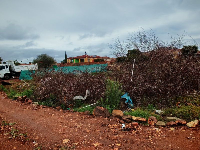 A view of an undeveloped residential plot featuring a dirt access road and overgrown vegetation, situated in a suburban neighborhood.