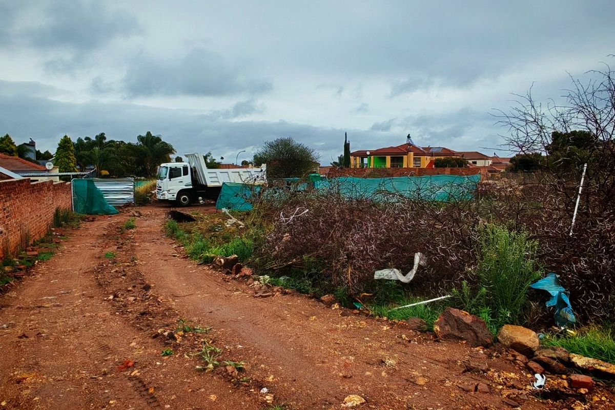 A view of a vacant residential plot featuring a dirt access road and existing brick boundary walling.