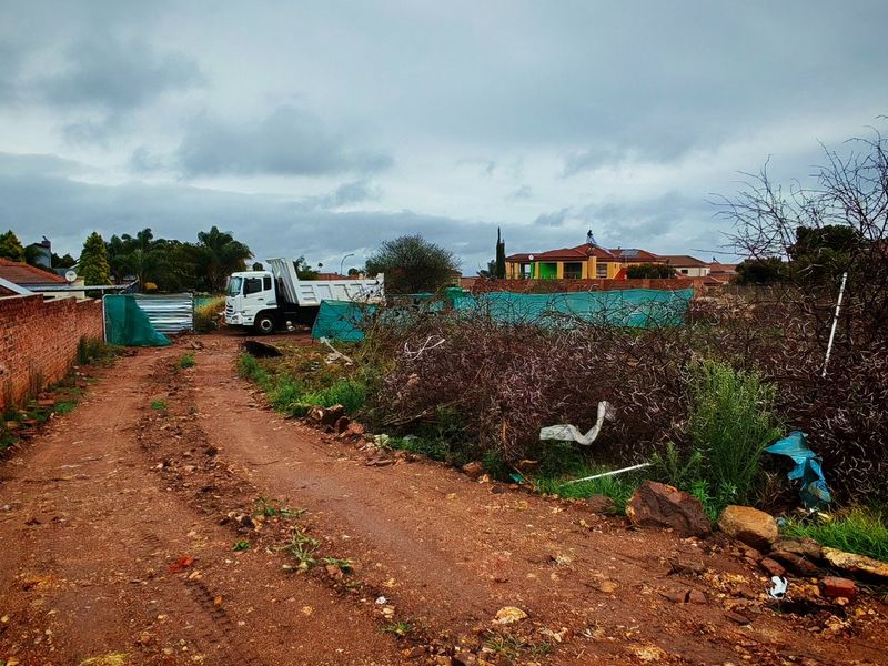 A view of a vacant residential plot featuring a dirt access road and existing brick boundary walling.