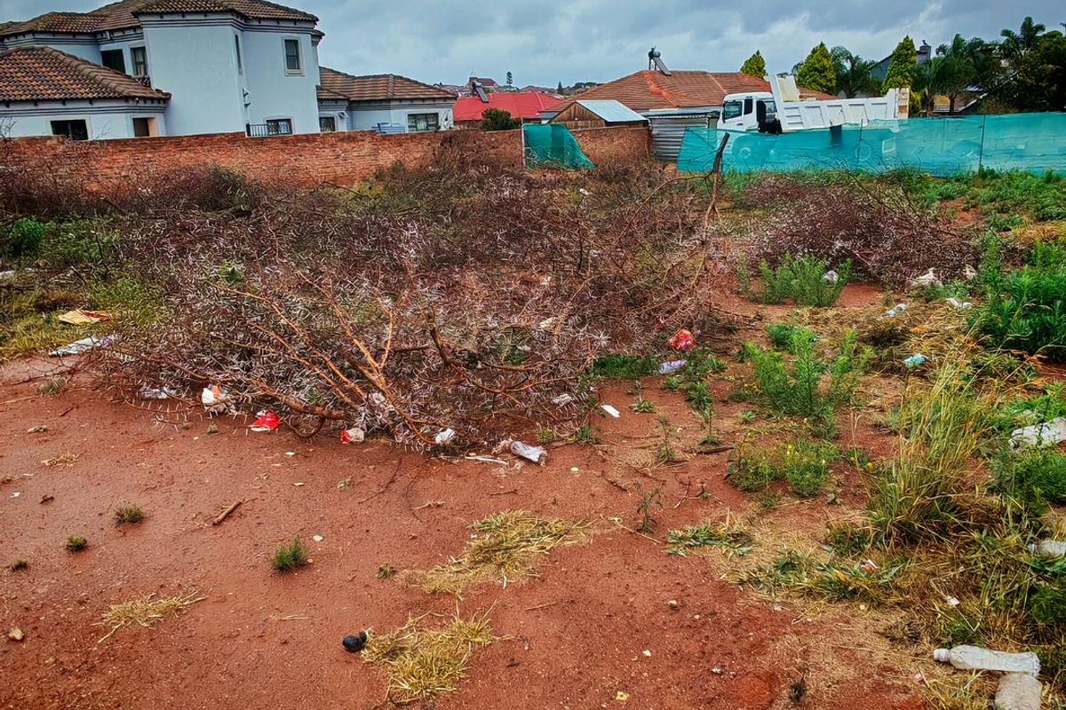 A vacant residential plot featuring a brick boundary wall and green shade cloth fencing, currently requiring site clearing and debris removal.