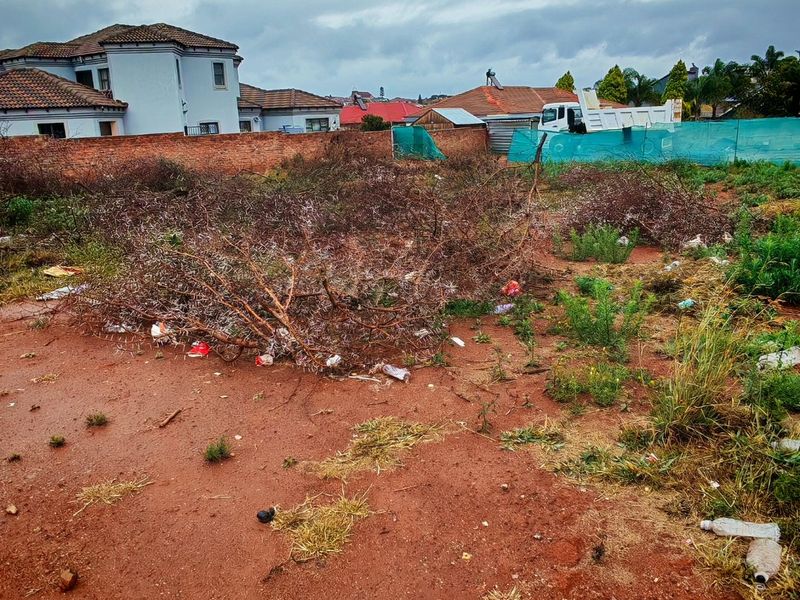 A vacant residential plot featuring a brick boundary wall and green shade cloth fencing, currently requiring site clearing and debris removal.