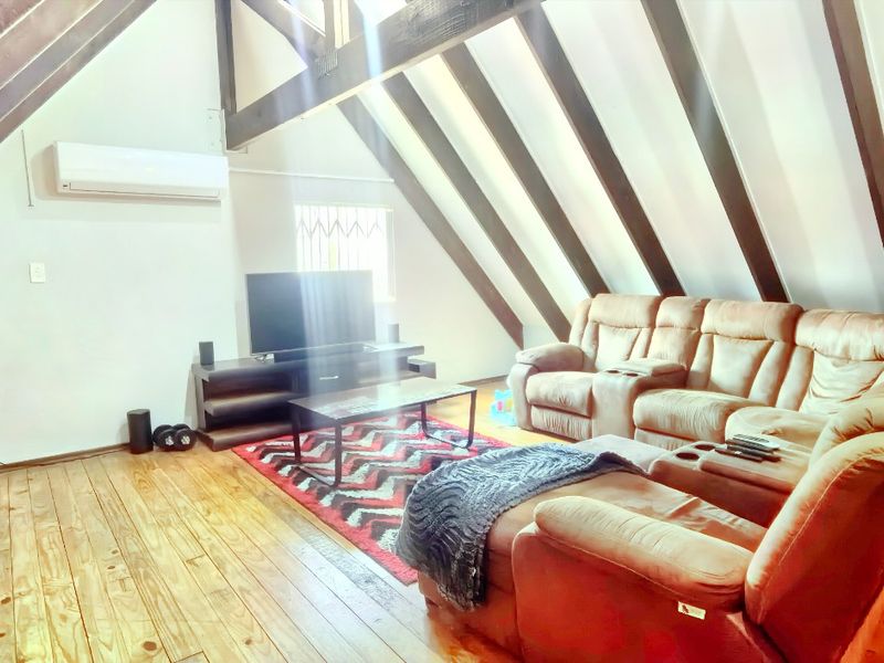 Spacious living room featuring a vaulted ceiling with exposed timber rafters, timber flooring, and a wall-mounted split-system air conditioner.