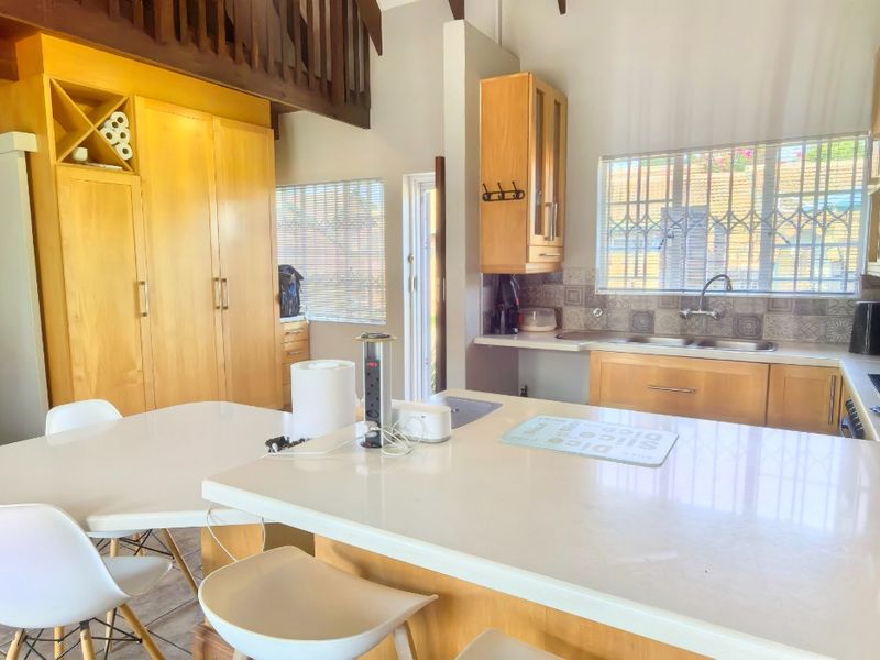 Open plan kitchen featuring wooden cabinetry, a central island, and a mezzanine level, with tiled flooring and natural light from windowed areas.