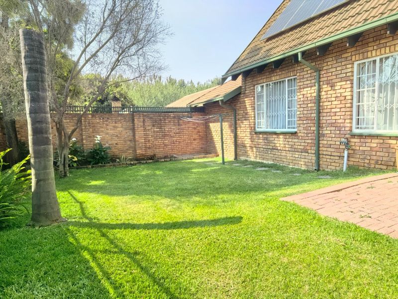 A private rear garden featuring a brick-paved patio area, established lawn, and secure perimeter walling, with solar panels installed on the roof.