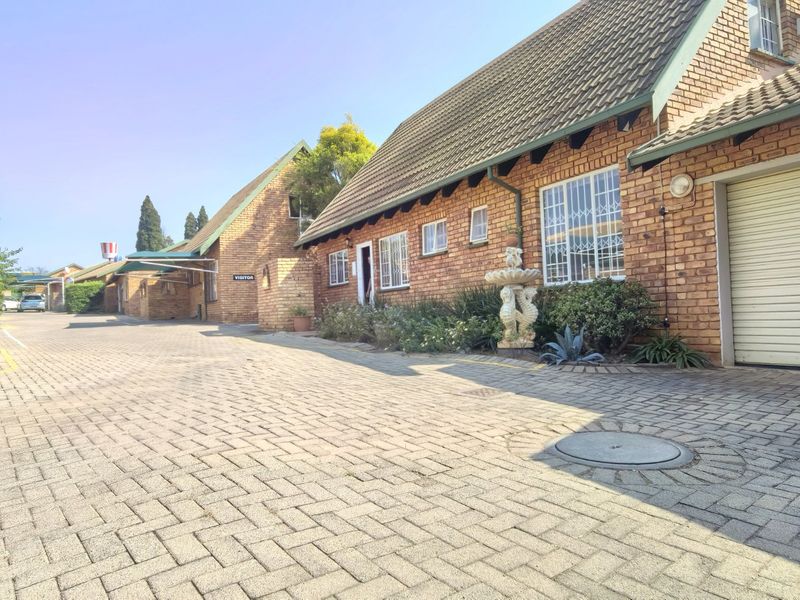 A view of the front exterior of a brick-faced residential property featuring a paved driveway, garage, and established garden elements.
