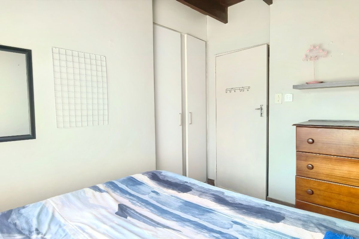 A bedroom featuring built-in wardrobe storage and exposed timber ceiling beams, providing a functional space with neutral wall finishes.