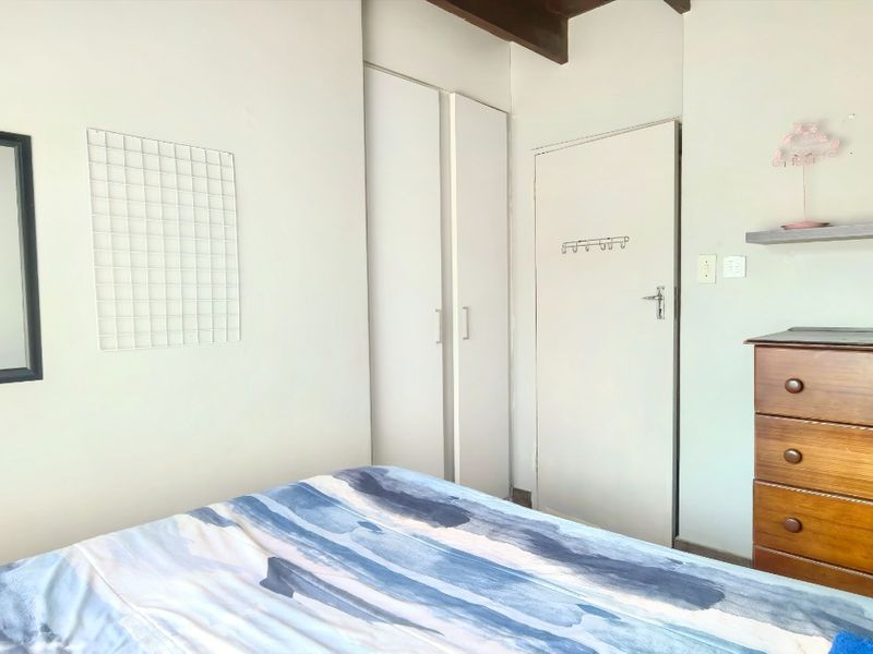 A bedroom featuring built-in wardrobe storage and exposed timber ceiling beams, providing a functional space with neutral wall finishes.
