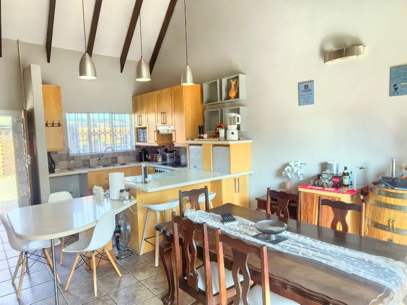 Open-plan living and dining area featuring a kitchen with timber cabinetry, vaulted ceilings with exposed beams, and tiled flooring throughout.