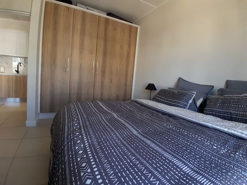 A well-maintained bedroom featuring a large built-in wooden wardrobe and neutral tiled flooring, with a view into the adjacent kitchen area.