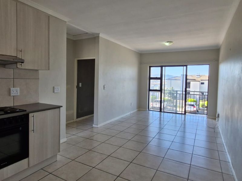 Open-plan kitchen and living area featuring tiled flooring, built-in cabinetry, and a sliding glass door leading to a balcony.