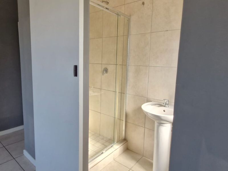 A functional bathroom featuring a pedestal basin and a glass-enclosed shower with neutral wall and floor tiling.
