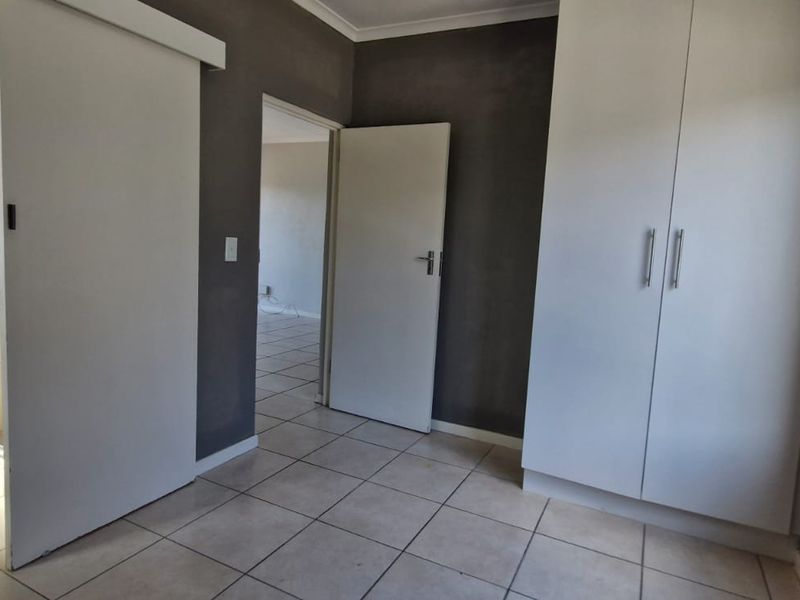 A spacious bedroom featuring tiled flooring, built-in cupboards, and an en-suite bathroom with a shower and pedestal basin.