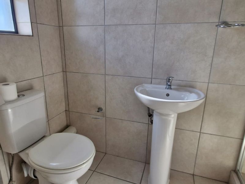 A clean and functional bathroom featuring a pedestal basin, toilet, and a glass-enclosed shower with neutral ceramic tiling throughout.