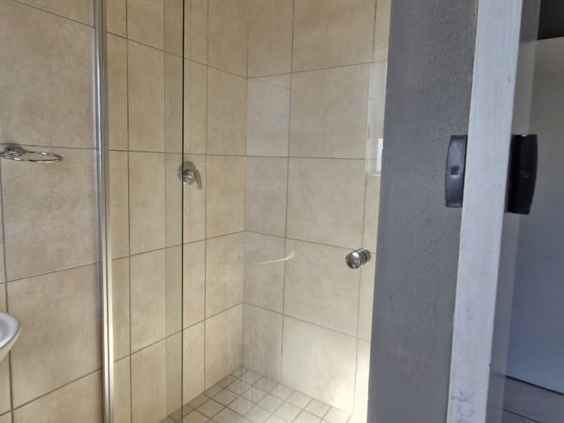A clean, functional bathroom featuring a pedestal basin with chrome mixer tap and a tiled shower enclosure with a glass door.