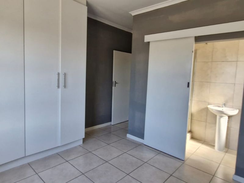 A clean bedroom featuring built-in cupboards, tiled flooring, and an en-suite bathroom with a pedestal basin accessed via a sliding door.