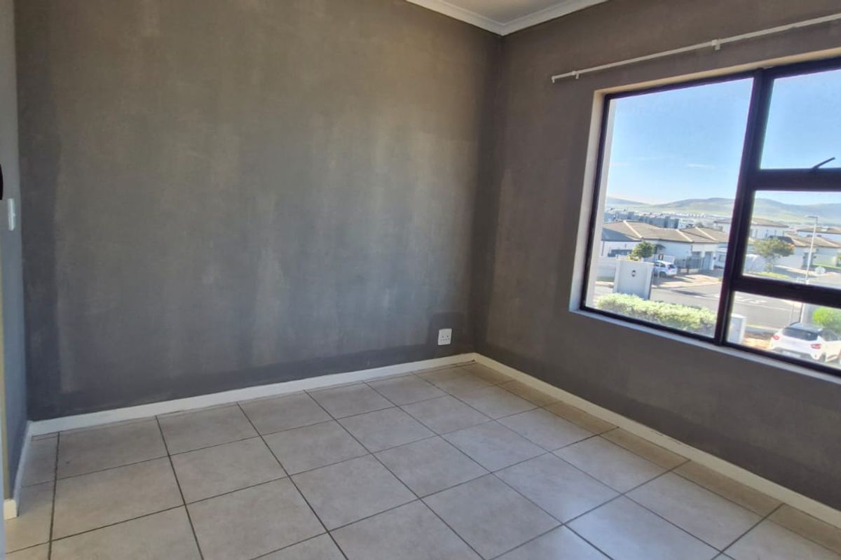 A vacant bedroom featuring neutral tiled flooring, grey painted walls, and an aluminium-framed window with natural light.
