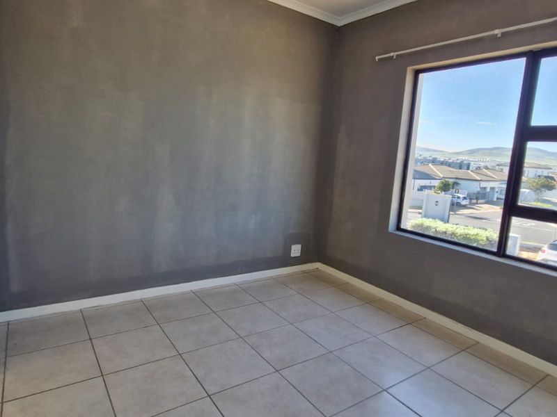 A vacant bedroom featuring neutral tiled flooring, grey painted walls, and an aluminium-framed window with natural light.