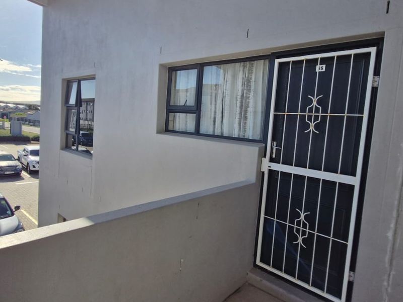 Exterior view of an apartment entrance featuring a security gate, aluminium window frames, and a wall-mounted fire extinguisher.