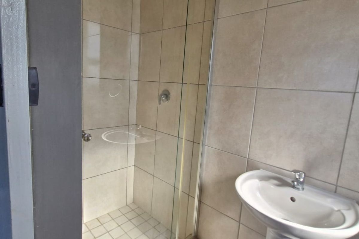 A clean, functional bathroom featuring a glass-enclosed shower, pedestal basin with chrome mixer tap, and neutral ceramic wall tiling.