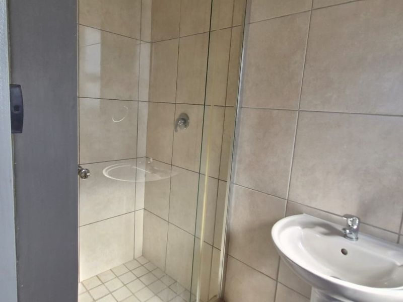 A clean, functional bathroom featuring a glass-enclosed shower, pedestal basin with chrome mixer tap, and neutral ceramic wall tiling.