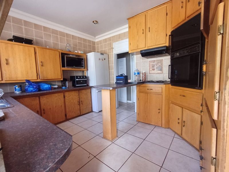 A functional kitchen featuring extensive wooden cabinetry, built-in double ovens, a breakfast bar, and tiled flooring, offering significant potential for a modern renovation.
