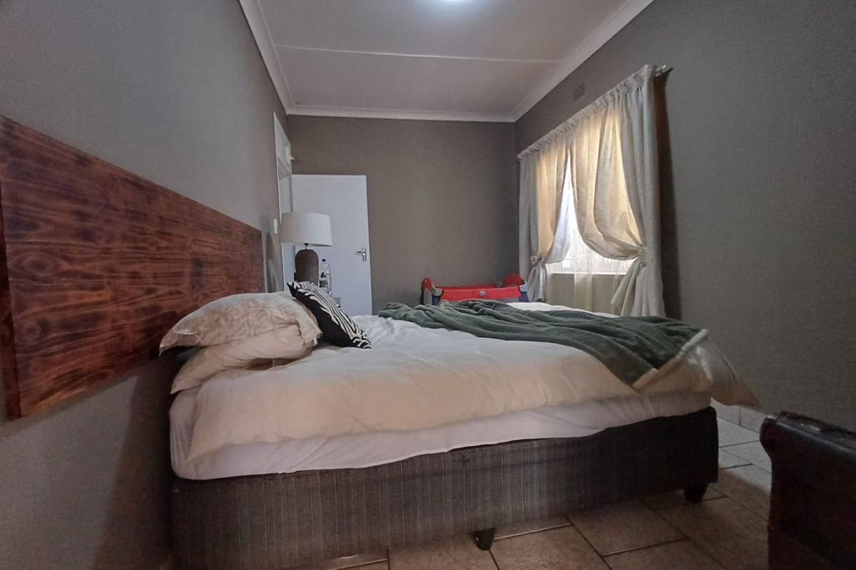 A bedroom featuring tiled flooring, a wooden headboard feature, and neutral wall tones, providing a functional space for rest.