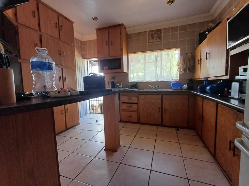 A dated kitchen featuring extensive wooden cabinetry, tiled flooring, and a functional layout with a breakfast bar and direct access to the exterior.