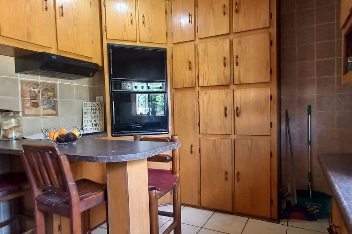 A functional kitchen featuring extensive built-in wooden cabinetry, tiled backsplash, integrated oven, and a breakfast bar area with tiled flooring.