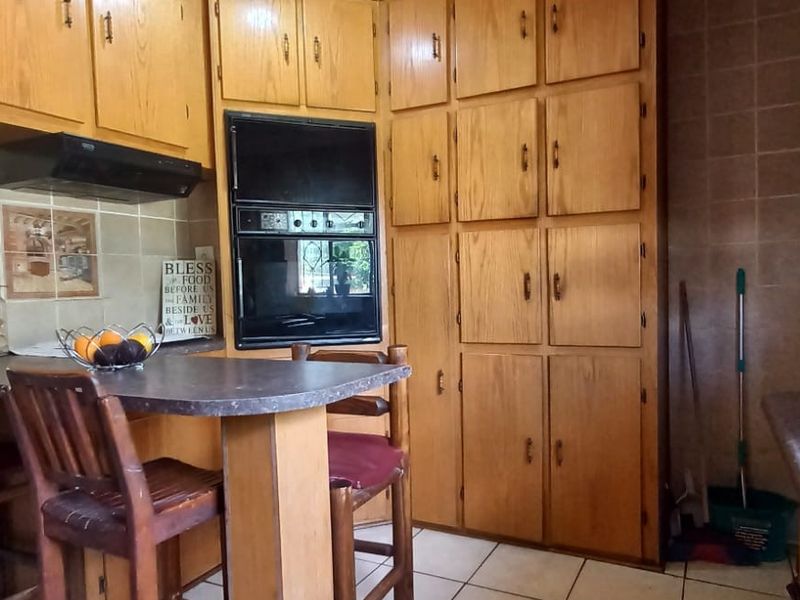 A functional kitchen featuring extensive built-in wooden cabinetry, tiled backsplash, integrated oven, and a breakfast bar area with tiled flooring.