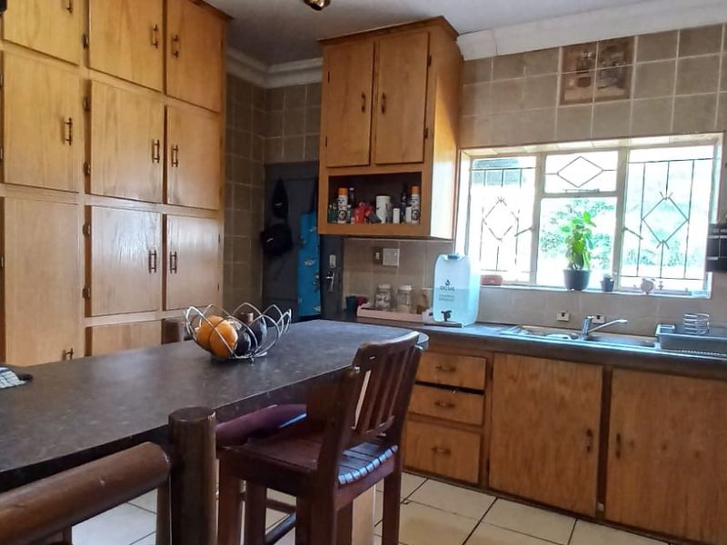 A dated kitchen featuring extensive wooden cabinetry, laminate countertops, a double sink, and tiled backsplash, offering significant potential for a modern renovation.